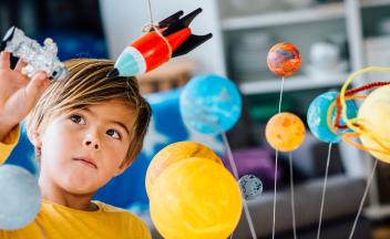 Young boy fascinated by models of a space rocket, astronaut and the planets