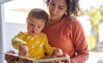 toddler pointing to words in a picture book while sitting on mother's lap