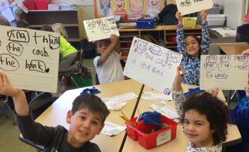 Elementary kids holding up word study examples in class