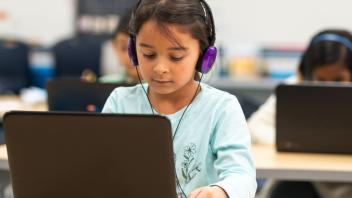 Young Latina student using a laptop with headphones