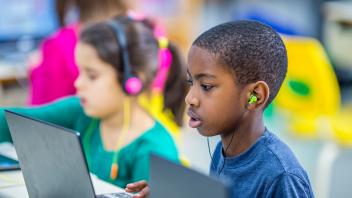 two young children using laptops and headphones in class