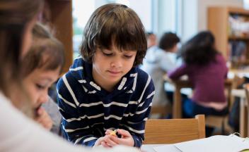 elementary boy concentrating on classroom task with teacher