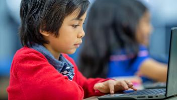 Latino first grader reading on tablet in classroom