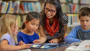 Elementary teacher sharing nonfiction book with 3 students around a table